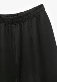 Svarta bomullsbyxor med elastisk midja, slät textur och detalj vid sid sömmarna. Enkel design, passar bra för avslappnad användning.