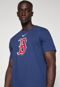 T-shirt in cotone blu navy con grande logo rosso "B" contornato di bianco, piccolo swoosh Nike bianco sul petto e scollo rotondo classico.
