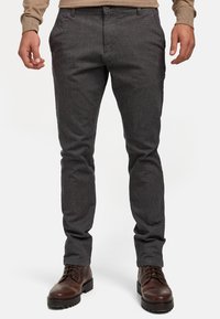 Pantalon gris texturé, à coupe slim, avec poches avant, fermeture à bouton, assorti à des bottes en cuir marron.