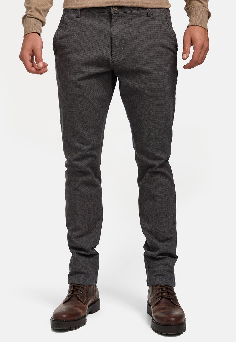Pantalon gris texturé, à coupe slim, avec poches avant, fermeture à bouton, assorti à des bottes en cuir marron.