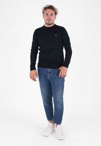 Maglione nero a maniche lunghe con collo rotondo, abbinato a jeans blu slim-fit e sneakers bianche. Design semplice, senza motivi o dettagli visibili.