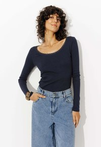 Haut à manches longues marine avec un décolleté scoop bordé de dentelle associé à un jean en denim bleu taille haute, présentant une coupe décontractée et des poches frontales.