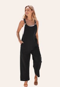 Combinaison en lin noir avec des jambes larges, des bretelles réglables et des boutons en bois. Présente une coupe décontractée et un design minimaliste.