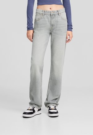 Jean droit gris clair avec une texture délavée, cinq poches et des coutures surpiquées, associé à des baskets noires et blanches.