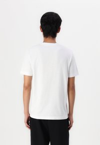 T-shirt bianca in cotone con maniche corte, colletto rotondo e vestibilità comoda. Il retro presenta una superficie liscia senza grafiche o motivi.