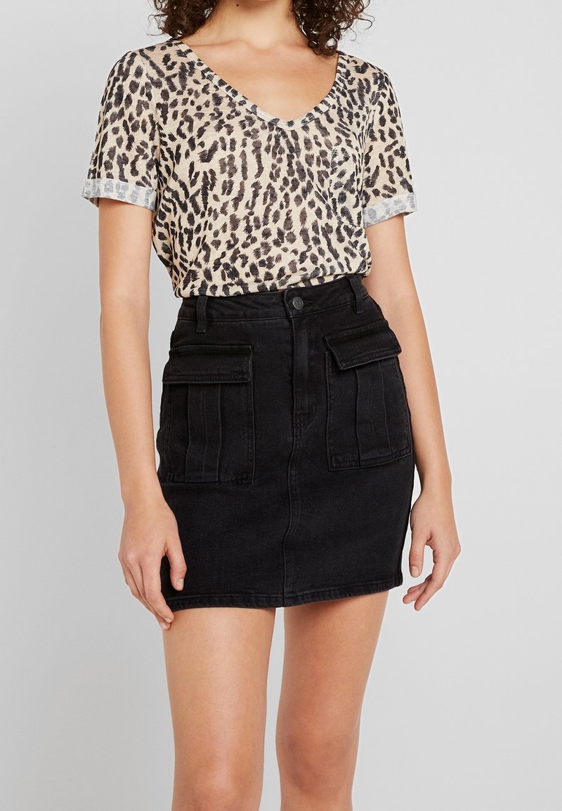 Top de manga corta con estampado de leopardo y escote en V, combinado con una falda de mezclilla negra que presenta bolsillos frontales y una silueta ajustada.