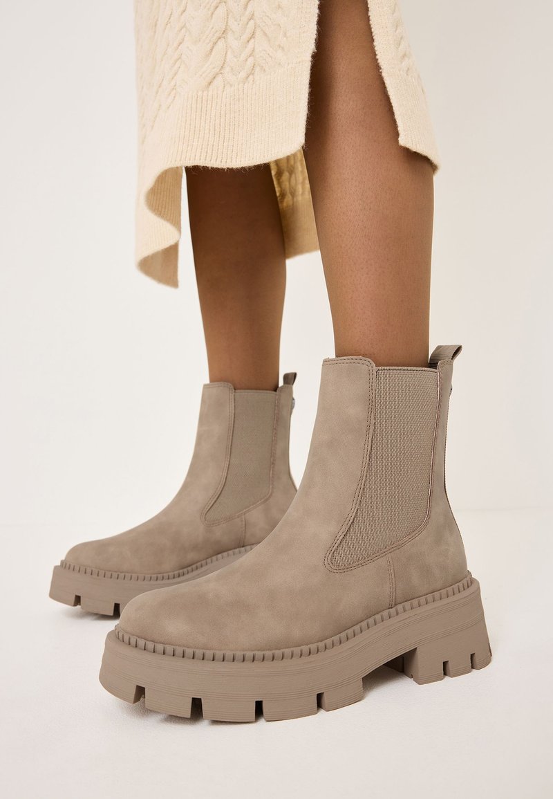 Tan faux suede ankle boots with elastic side panels, chunky rubber soles, and ribbed accents. Designed with a rounded toe and pull tab.