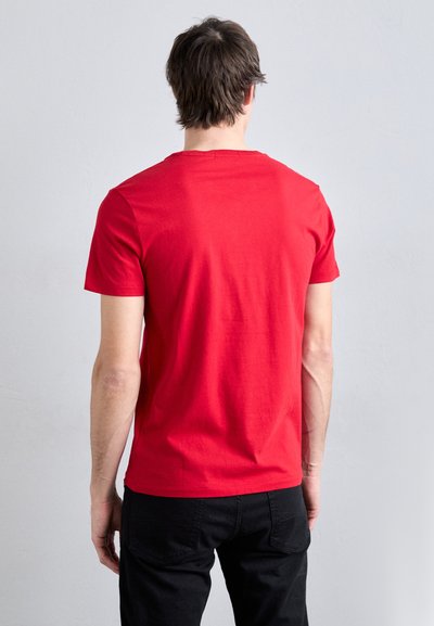 Piros pamut póló rövid ujjal, kerek nyakkivágással és sima textúrával. Fekete nadrággal viselve, hátulról nézve.