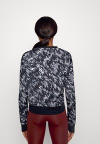 Schwarzes und graues, gemustertes sportliches Sweatshirt mit langen Ärmeln, gerippten Bündchen und Saum. Hat eine glatte, glänzende Textur.