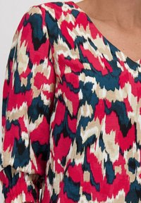 Multikleurige blouse met een cheeta-achtig print in tinten roze, blauw en beige. De stof heeft een zachte, gladde textuur en een V-halsontwerp.