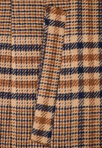 Tkanina tweed w wzór w zęby psa, w odcieniach brązu, beżu i granatu, o miękkiej teksturze i widocznym detalu kieszeni.