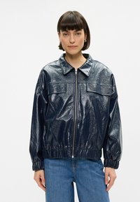 Jūras spēku zila spīdīga bomberjakete ar rāvējslēdzēju priekšpusē, apkakles kaklu un divām krūšu kabatām. Tai ir elastīgi aproces un brīva piegriezuma forma.