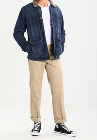 Džínová bunda s chlupatým límcem, pod ní bílá košile, béžové kalhoty a černé vysoké tenisky s bílými detaily.