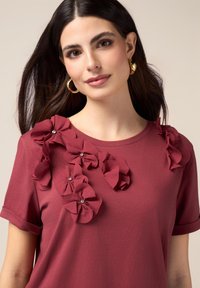 Bordeauxfarbenes T-Shirt mit kurzen Ärmeln, das aus strukturiertem Stoff gefertigt ist und mit auffälligen floralen Applikationen mit Edelsteinakzenten auf den Schultern versehen ist. Mit glatter Oberfläche und lässiger Passform.