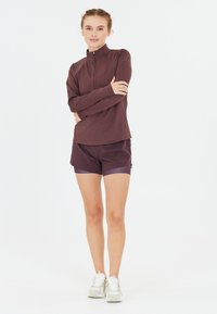 Langsleeve, ritssluiting top in donker bordeaux, gecombineerd met bijpassende shorts. De stof lijkt glad en rekbaar, met een subtiele glans.