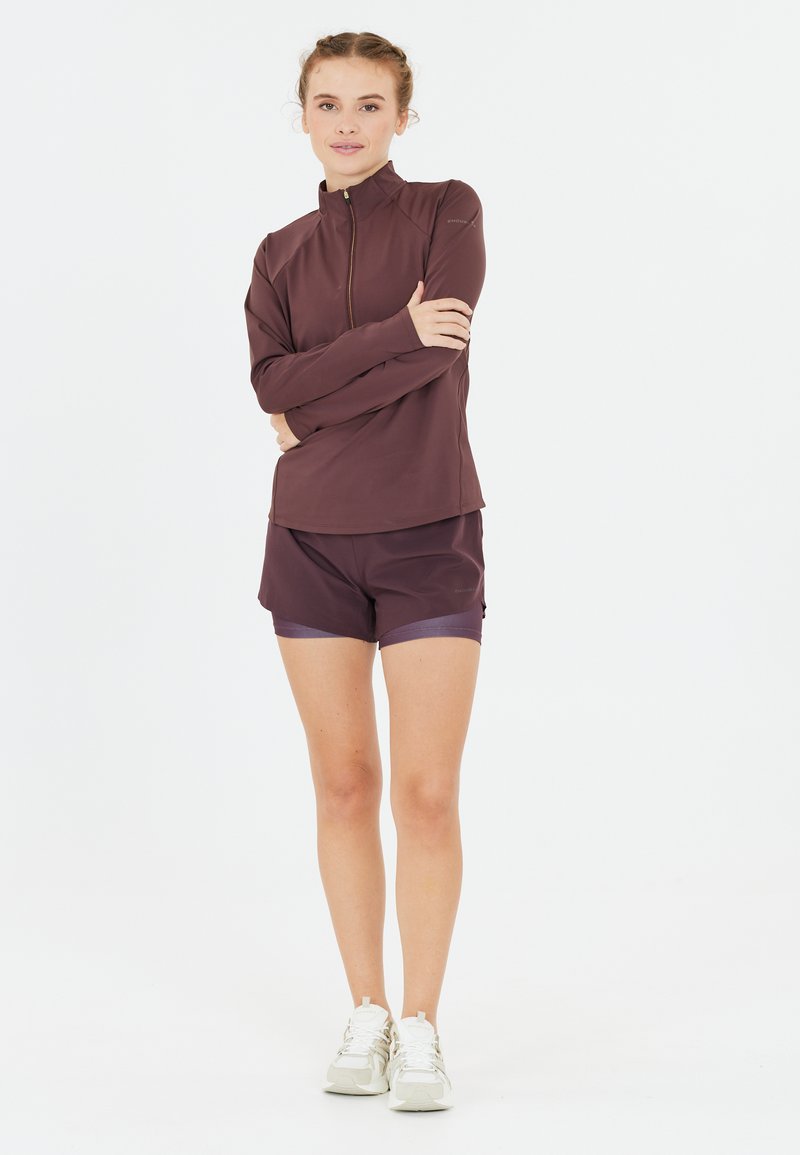 Langsleeve, ritssluiting top in donker bordeaux, gecombineerd met bijpassende shorts. De stof lijkt glad en rekbaar, met een subtiele glans.