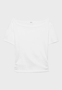 Bela kratka majica z odkrito ramo in zloženkami na straneh, prikazana na enostavni svetlo sivi podlagi.