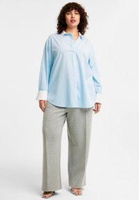 Ljusblå randig skjorta med vit krage, matchad med avslappnade grå sweatpants. Outfiten har vida ben och mjukt material.