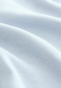 Himmelsblau bomullstyg med en slät textur, uppvisad i milda veck som avslöjar ett fint, stickat mönster genom hela.