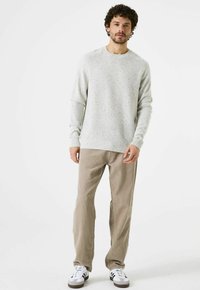 Hellgrauer, strukturierter Strickpullover mit gerippten Bündchen und Saum, kombiniert mit beigen Cordhosen und weißen Turnschuhen mit schwarzen Streifen.