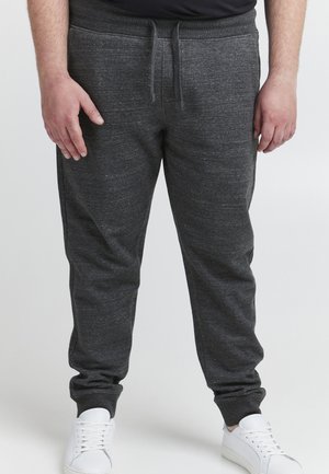 Pantalone od jogger stila u boji ugljena s teksturiranim materijalom, elastičnim strukom, zatvaranjem na vezicu i sužavajućim manžetama, u kombinaciji s bijelim tenisicama.