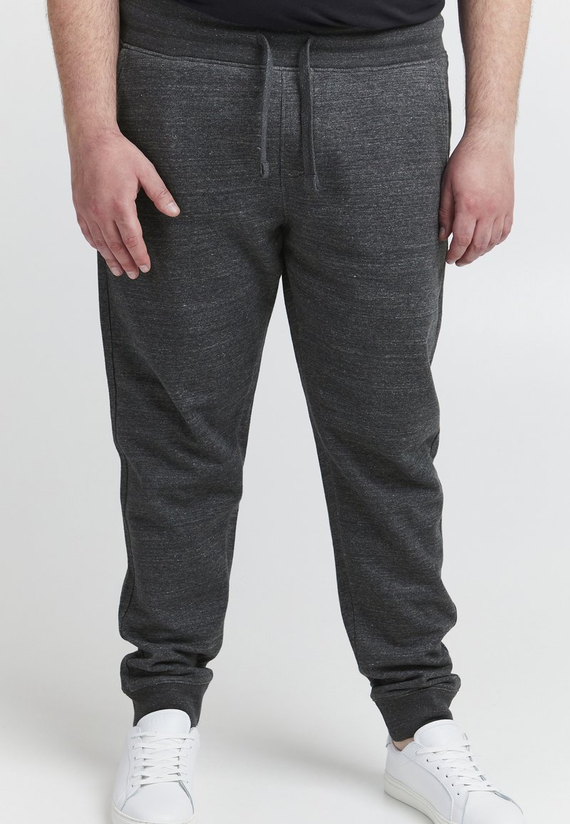 Kulsorte joggers med struktureret stof, elastisk talje, snøre lukning og tætsiddende cuffs, parret med hvide sneakers.