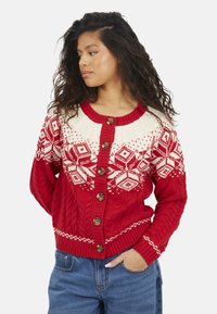 Cardigan rosso lavorato a maglia a trecce con motivi geometrici bianchi, caratterizzato da scollo arrotondato e bottoni marroni, polsini e orlo a coste.