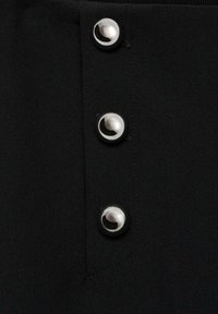 Tissu noir avec trois boutons-pression argentés sur le côté, présentant une texture lisse et des détails de piqûre serrée autour des trous de boutons.