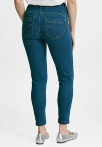 Modré denimové skinny džíny s vysokým pasem, vybavené dvěma zadními kapsami a srolovanými lemy. Tkanina má hladkou, mírně elastickou strukturu.