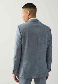 Svijetloplavi sako odijela s glatkom teksturom, uskog kroja, i jednim prorezom na leđima; sadrži elegantne reveri i detalje na gumbima.