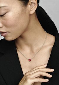 Strieborný náhrdelník s pendantom v tvare srdca z červeného drahokamu. Reťaz je jemná a pendant má prstenové osadenia.