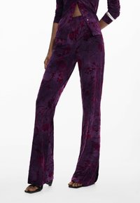 Pantalons évasés en velours violet avec un motif floral dans des teintes plus foncées de rouge. Le tissu a une texture lisse et un léger éclat.