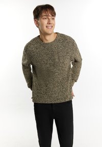 Maglione lavorato a maglia con texture in tonalità terra, dotato di scollo rotondo e vestibilità rilassata. Abbinato a pantaloni neri a gamba dritta.