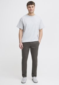 Maglietta in cotone grigia a maniche corte, abbinata a pantaloni verde scuro e sneaker grigie chiare, caratterizzata da una vestibilità comoda e un design semplice.