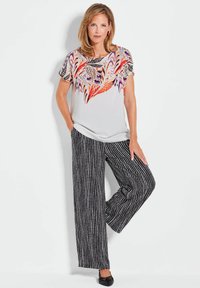 Lichtgewicht, kortgewoven top met een kleurrijk veerpatroon en een effen witte basis, gecombineerd met zwart-wit gestreepte wijde broek.