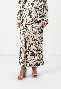 Gonna lunga e fluida in un tessuto leggero con un motivo astratto nero e verde su fondo crema, abbinata a sandali con tacchi alti beige.