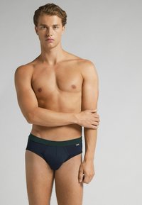 Mörkblå kalsonger med ett grönt midjeband, tillverkade av mjukt tyg. Designen har sömmar och en åtsittande passform som sitter över höften.