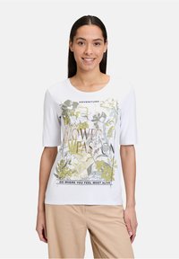 Hvid kortærmet t-shirt med et blomstret grafisk tryk i grøn og gul, med tekstelementer og rund halsudskæring.