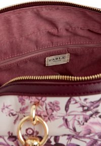 Vinyl-Innenfutter in Rosa, mit einem Reißverschlussfach und einem Etikett mit der Aufschrift "FABLE ENGLAND". Goldener Reißverschluss und Hardware betonen das florale Muster auf der Außenseite.