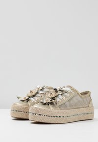 Zapatillas de malla dorada con embellishments florales, suelas de plataforma de yute y detalles iridiscentes a lo largo de la suela. Diseño de cordones.