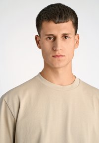 Beige kortærmet t-shirt med rund halsudsk�æring, lavet af et glat stof. Pasformen er afslappet, med minimale sømme og en diskret tekstur.