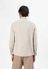 Camisa de manga longa bege clara com um padrão texturizado, punhos com botões e um colarinho clássico, combinada com calças listradas bege a condizer.