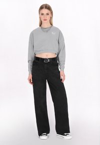 Szürke, rövidített kapucnis pulóver görkorcsolya grafikával, magas derekú fekete, bő szárú farmernadrággal és fekete sneakers-szel, fehér talppal párosítva.