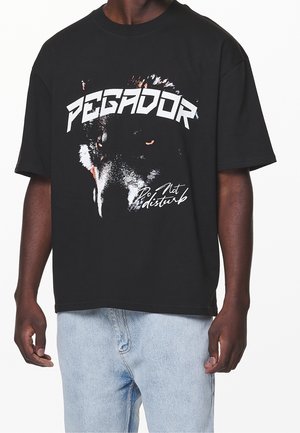 Black cotton t-shirt featuring a graphic wolf design with the text "PEGADOR" above and "Do Not Disturb" below. Short sleeves, relaxed fit.