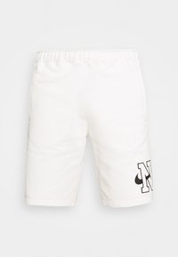 Vita bomullsshorts med elastisk midja, sidfickor och en stor svart grafisk bokstav "N" på nedre sidan. Mjukt material.