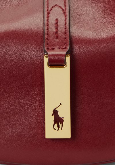 Curea din piele maroon pentru geantă, cu un tag metalic dreptunghiular auriu, ce prezintă o siluetă întunecată a unui cal și a unui călăreț, ilustrând o măiestrie detaliată.