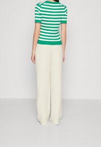 Top a righe verdi e bianche in maglia con maniche corte, abbinato a pantaloni beige a gamba larga; texture liscia e design aderente in vita.