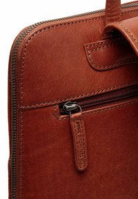 Sac en cuir marron avec une finition texturée, équipé d'une poche zippée à l'avant et d'une tirette de fermeture éclair durable. Les bords de couture sont visibles.