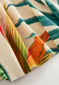 Tissu avec un fond beige présentant des rayures vertes et des motifs floraux tropicaux colorés, montré en gros plan avec des plis et des détails de texture.