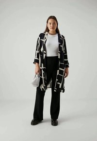 Black and white patterned kimono jacket with a loose fit, worn over a white top and black pants, complemented by a small bag.